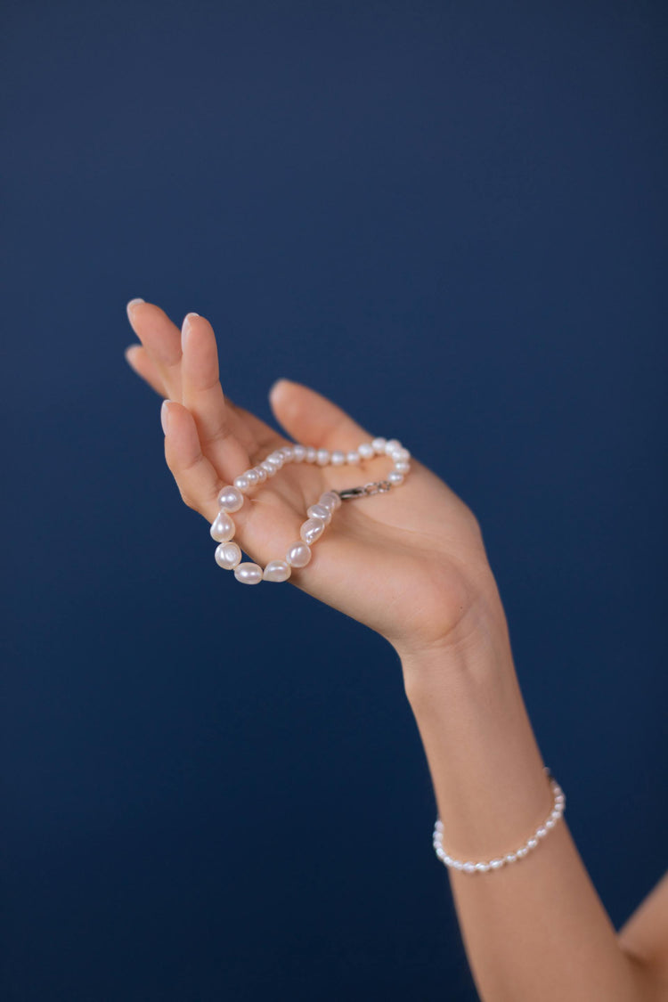 This is a photo of a woman's hand holding a baroque pearl bracelet against a dark blue background.