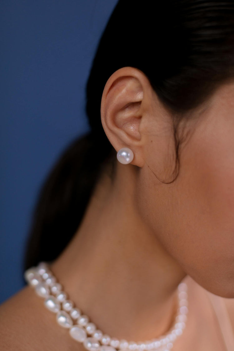 This is a photo of a woman's face wearing a white pearl earring against a dark blue background.