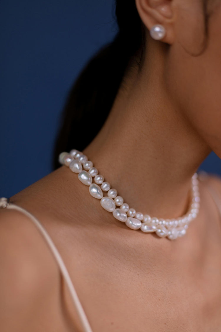   This is a photo of a woman's face wearing a white pearl necklace against a dark blue background.